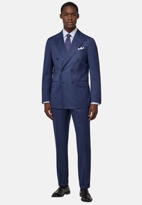 Giacca blu navy doppiopetto con vestibilità su misura, rever a punta e tasche laterali. Abbinata a una camicia a righe chiare e una cravatta a fantasia.