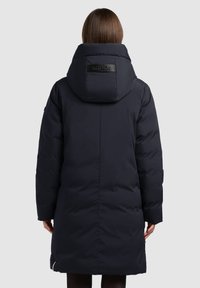 Mornarski pufasti kaput s velikom kapom, qiltanom teksturom i logotipom na stražnjoj strani. Ima dizajn srednje dužine i manžete na rukavima.