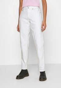 Weiße Denim-Hosen mit hohem Bund und geradem Bein, mit einem Knopfverschluss und fünf Taschen. Kombiniert mit schwarzen Schnürstiefeln.