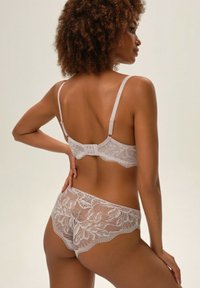 Koronkowy biustonosz i dopasowane majtki w jasnoróżowym kolorze, ozdobione kwiatowymi wzorami, z falbaniastymi krawędziami, regulowanymi ramiączkami i zapięciem na haczyk.