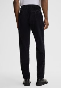 Dark narrow corduroy pants with a textured finish, featuring back pockets and a classic fit, paired with black footwear.