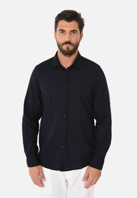 Camicia a maniche lunghe blu navy con colletto, texture semplice e bottoni abbinati, abbinata a pantaloni chiari.