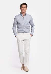 Chemise à boutons de couleur bleu clair avec un motif floral blanc, associée à un pantalon couleur crème et des mocassins beiges. Texture lisse et coupe ajustée.