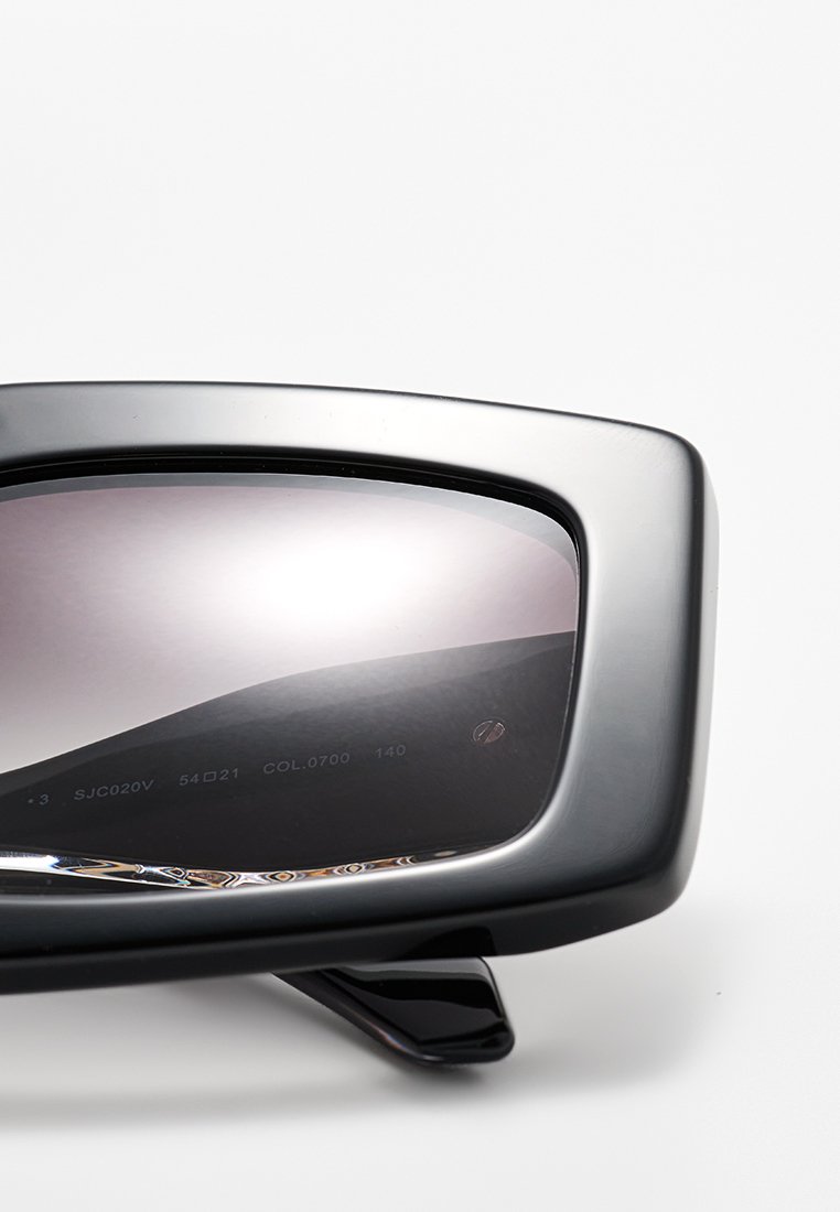 Schwarze, übergroße Sonnenbrille mit hochglänzender Oberfläche, abgedunkelten Gläsern und eckigem Rahmendesign. Bedruckte Details auf dem Glas.