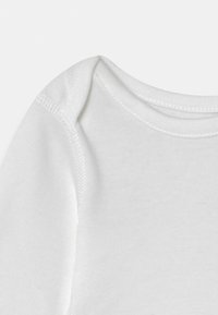 Vit bomullsompong med rund hals och korta ärmar. Har rena, platta sömmar och en slät yta. Enkel design utan mönster.