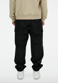 Pantalons cargo noirs avec des poignets élastiques, dotés de poches latérales et d'une coupe décontractée, associés à des chaussures de sport blanches.
