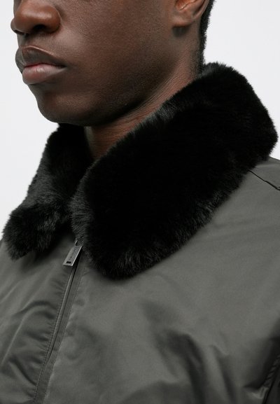 Schwarze Bomberjacke mit einem Kragen aus Kunstfell. Sie verfügt über eine glatte Stofftexture und einen Reißverschluss auf der Vorderseite.
