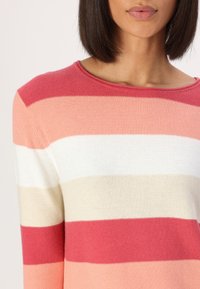 Pull en tricot avec des rayures horizontales corail, rose, blanc et beige. Col rond et texture douce. Vue du haut du corps.