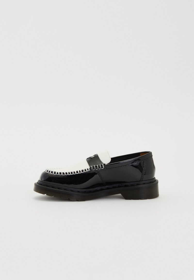 Mocassin en cuir noir et blanc avec des détails cousus, une semelle épaisse et une sangle à penni, présenté sur un fond clair simple.