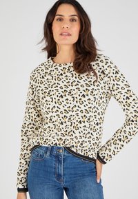 Maglione zebrato in crema, con accenti neri e dorati, polsini a costine e scollatura rotonda; abbinato a jeans blu.