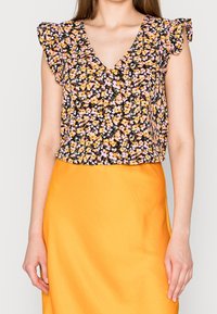 Haut à imprimé floral sur fond noir, ornée de fleurs roses et jaunes. Manches courtes à volants et design en V. Associé à une jupe orange vif.