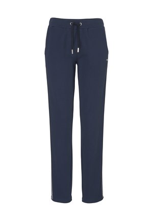 Bareback-Person, die auf einem Fuß steht und marineblaue Hosen mit hellgrauen Seitenstreifen und elastischem Bund trägt, Hände in den Taschen.