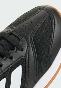 Chaussure de sport noire avec un dessus en tissu texturé, des accents en cuir et des rayures blanches. La semelle en caoutchouc gomme assure adhérence et durabilité.