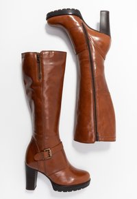 Bottes montantes en cuir marron avec finition brillante, dotées d'une fermeture éclair latérale, d'un accent boucle, et d'un talon haut épais. Semelle texturée.