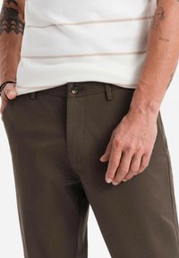 Pantalon texturé marron avec fermeture à bouton, doté de passants de ceinture et d'une coupe slim, associé à un haut en tricot rayé blanc.