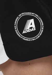 Svart och vitt tyg med en cirkulär Adidas-logotyp som har ett stort "A" och text om varumärket på engelska, tyska och franska.