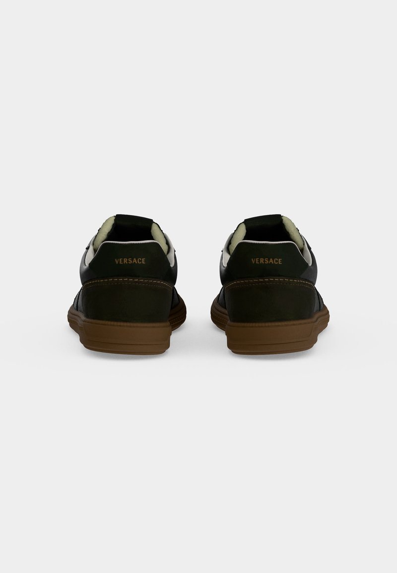 Coppia di sneakers basse nere e marroni con interno imbottito bianco, viste da dietro che mostrano il logo "Versace" sulle linguette del tallone.