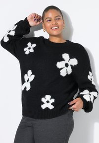 Zwarte gebreide trui met grote witte bloemmotieven. Losse pasvorm met geribbelde manchetten en zoom. Zachte textuur, ronde halslijn.