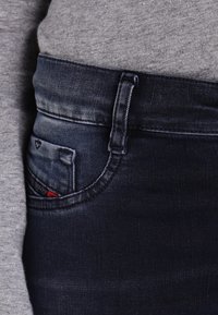 Tmavě modré džíny z denimu s mírným vyblednutím, s přední kapsou s červeným akcentem, precizním šitím a středním pasem.