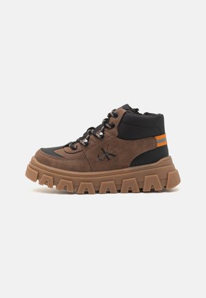 Baskets montantes marron et noir avec semelle épaisse, œillets métalliques, lacets et bandes orange à l'arrière, logo Calvin Klein sur le côté.