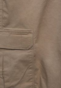 Brun tekstureret stof med en flad lomme, syede kanter og en subtil glans, der fremviser et simpelt design og rene linjer.