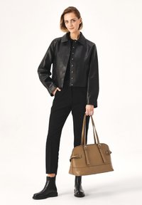Black leather cropped jacket, black fitted pants, black ankle boots, and a brown structured handbag with adjustable straps and hardware accents.