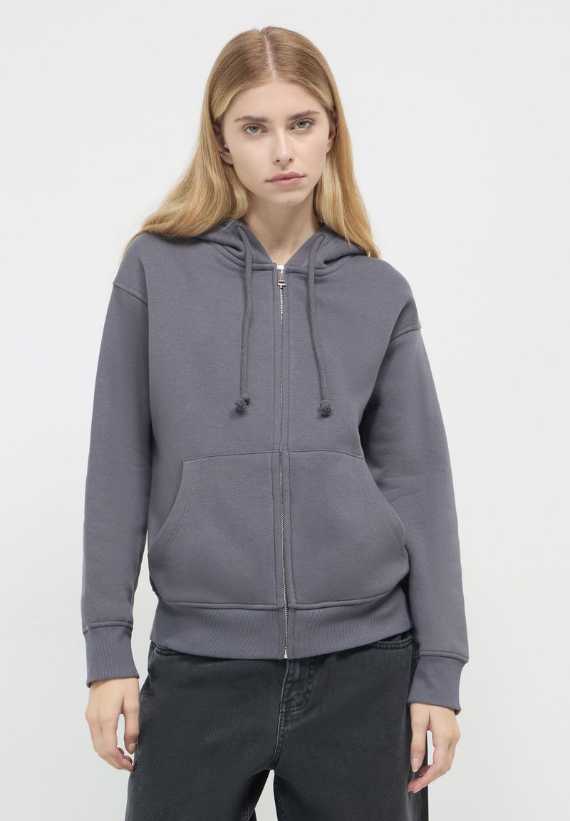 Felpa grigia con zip, cappuccio regolabile con coulisse, tasche frontali e polsini a costine. Realizzata in tessuto morbido con una consistenza liscia.