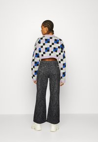 Suéter curto em roxo claro com quadrados multicoloridos; combinado com jeans pretos de perna larga com um padrão ondulado e ténis brancos robustos.