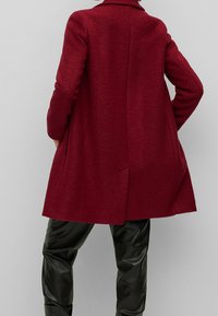 Rode wollen blend jas met een gestructureerde kraag, drop schouders en een uitlopende silhouet. Te combineren met aansluitende zwarte nep leren broek.