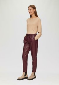 Beige lange mouwen top gecombineerd met bordeauxkleurige nep leren joggers met een elastische tailleband en voorzakken, compleet met tan enkellaarzen.