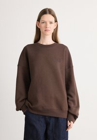 Brown sweatshirt made of soft fabric, featuring a crew neck and dropped shoulders. Displays simple embossed logo on the chest.