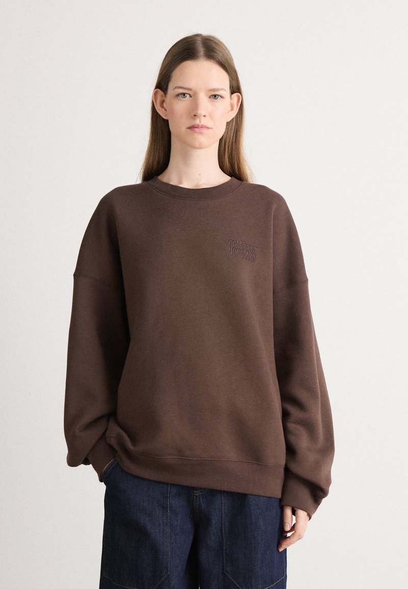 Brązowy sweatshirt wykonany z miękkiego materiału, z okrągłym dekoltem i obniżonymi ramionami. Posiada prosty wytłoczony logo na klatce piersiowej.