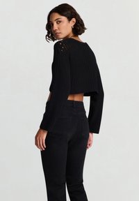 Maglione nero corto in maglia con texture a coste e dettagli con spalle scoperte, abbinato a jeans neri a vita alta con tasche sul retro.