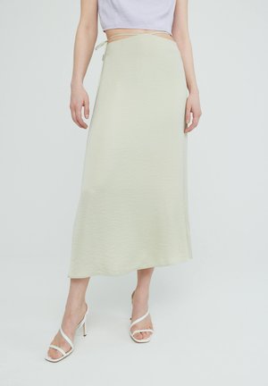 Lichtgroene, middellange rok met een gestructureerde stof, uitgerust met een striksluiting op de taille. Gecombineerd met witte sandalen met hoge hakken.