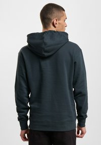 Kapuzensweatshirt in Dunkelgrün. Verfügt über ein strukturiertes Material, lange Ärmel und einen lockeren Schnitt. Verstellbarer Kordelzug an der Kapuze.