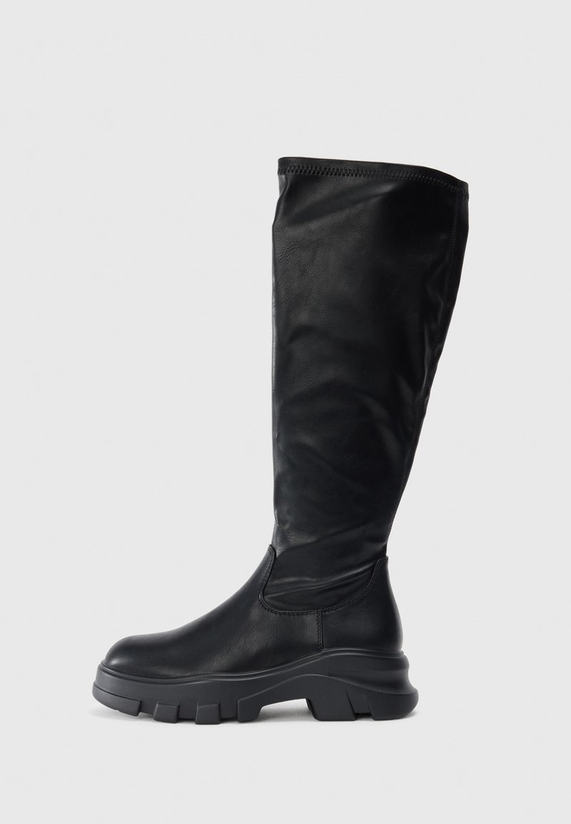 Botas negras hasta la rodilla hechas de cuero suave, con una suela de goma gruesa que ofrece un agarre texturizado y un diseño aerodinámico.