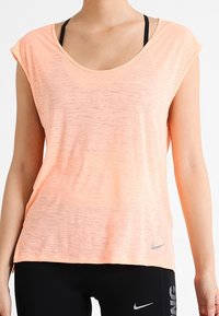 Camiseta deportiva ligera color melocotón con escote redondo, mangas cortas y una textura sutil. Cuenta con un pequeño logo gris de Nike en el frente.