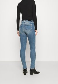 Passformade blå denimjeans med bakfickor, medelhögt midjeband och diskret slitningar. Kombineras med svarta klackstövlar och en långärmad topp.
