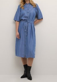 Denim-paita mekko lyhyillä hihoilla, napitus edessä, vyötärönauha, polvipituinen, vaaleansininen väri ja hienovaraiset ompeluyksityiskohdat saumoissa.