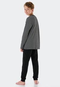 Camisa de manga larga a rayas blancas y negras combinada con pantalones negros lisos. La camisa tiene un escote redondo y un corte holgado.