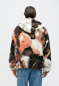 Felpa con cappuccio in pile marrone, arancione e crema con un motivo testurizzato e pattern. Presenta un cappuccio, polsini elasticizzati e una vestibilità comoda.