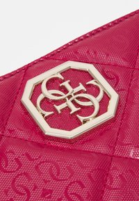 Lesklá růžová taška s prošívaným vzorem a zlatým osmihranným logem s propletenými písmeny G, H, C a O.