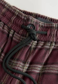 Bordeaux-geruite pyjamabroek met een geborstelde structuur, voorzien van een elastische tailleband, zwarte trekkoord en knoopsluiting.