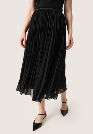 Gonna midi plissettata nera realizzata in tessuto leggero. Presenta una vita e fluisce fino all'orlo con una finitura trasparente, abbinata a scarpe nere a punta.