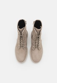 Vaaleanbeige kangastossut, joissa on sileä mokkajäljitelmä, pehmustettu nilkkareunus, vetoketjukiinnitys sivussa ja teksturoitu kumipohja.