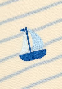 Blau-weiße Segelboot-Stickerei auf cremefarbenem Stoff mit hellblauen horizontalen Streifen.