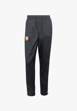 Pantalon de sport noir avec taille élastique, logo de Manchester United sur la cuisse gauche et détail d’un cordon vert à la cheville droite.