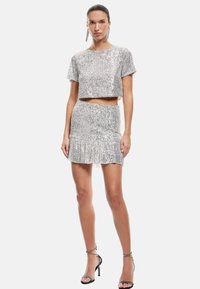 Zilveren pailletten crop top met korte mouwen, gecombineerd met een bijpassende mini-rok met franjes. Heeft een getailleerd ontwerp en een glanzende textuur.