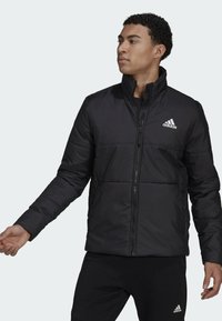 Giacca puffer nera con colletto alto, zip frontale e design trapuntato. Presenta il logo Adidas in bianco zona petto sinistra.