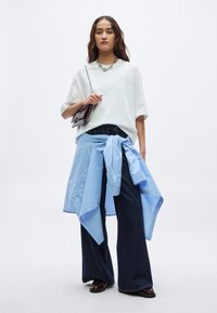 Balta pārliela izmēra T-krekls, tumši zilas zvārstu bikses un zilas svītrainas krekls, kas sasiets ap vidukli. Aksesuāri: tumša soma un sudraba kaklarota.